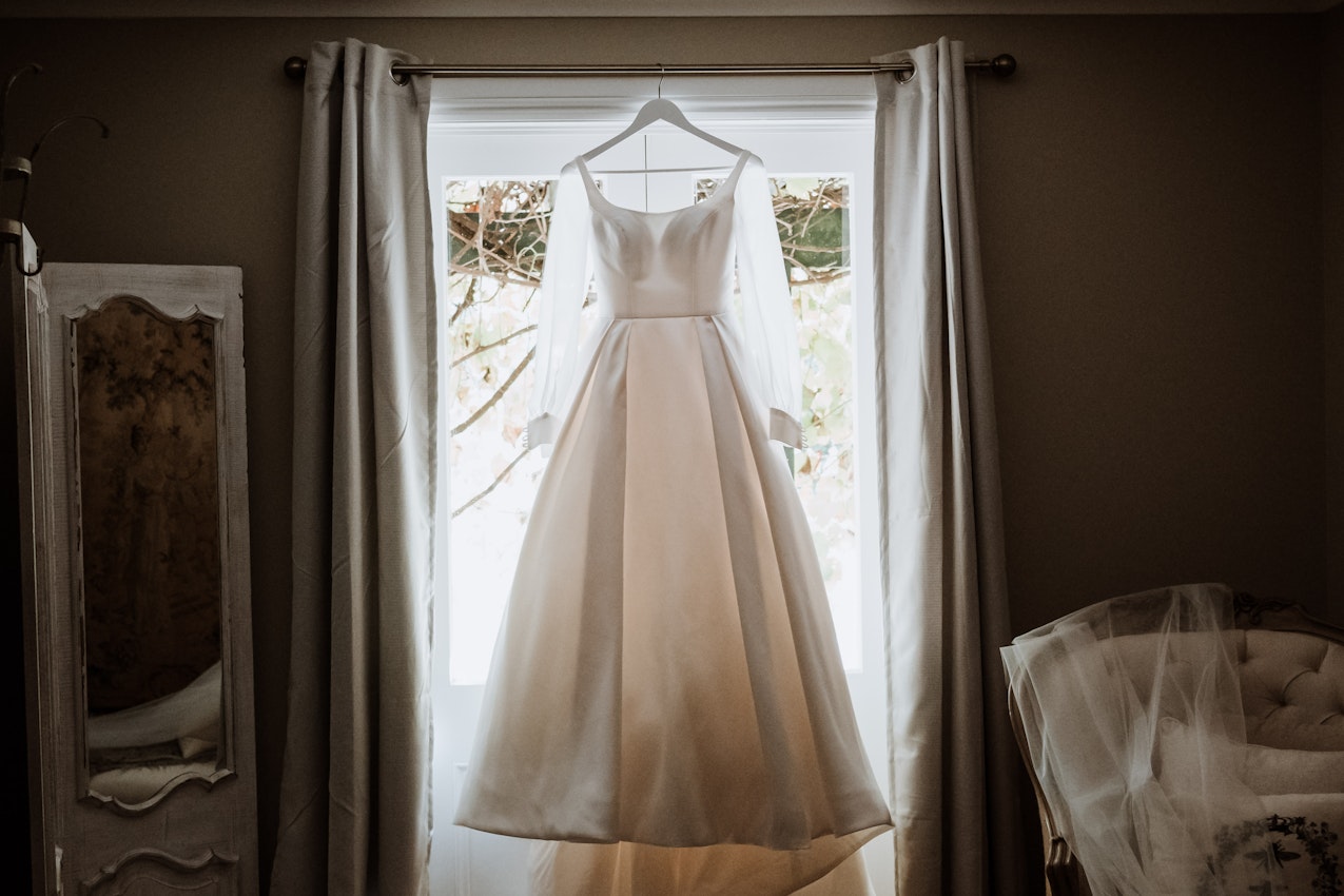 Wedding dress called Selena with personalized sleeves hanging in window.