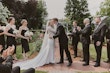 Bride and groom kissing while wedding party, all dressed in black, clap and cheer.