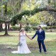 Bride and groom holding hands underneath trees and moss.