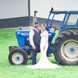 Bride wearing Drita wedding dress by Maggie Sottero with her husband in front of a tracktor