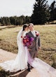 Bride Wearing Sexy Lace Wedding Dress Called Hazel By Rebecca Ingram Holding Vibrant Purple And Orange Bouquet