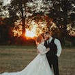Bride Wearing Lace Long-Sleeve Wedding Gown Called Raphael By Maggie Sottero With Groom In A Field