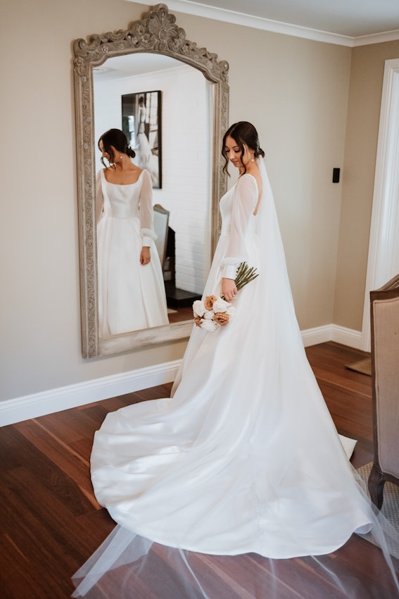Bride wearing wedding dress called Selena, stood in front of large mirror.