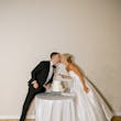 Bride wearing Zinaida by Maggie Sottero cutting the cake and kissing her husband
