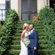 Bride kissing her groom on the cheek in front of stairs covered in greenery.
