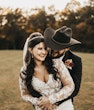 Bride Wearing Lacey Sheath Long Sleeve Wedding Dress Called Francesca By Maggie Sottero Held From Behind By Cowboy Hat Groom