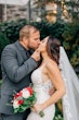 Groom Kissing Bride Wearing A Fitted Lace Wedding Dress Named Veronique by Maggie Sottero With A Veil And Bouquet Of Red And White Roses