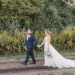 Bride wearing wedding dress called Pierce holding hands with groom walking along dirt path.