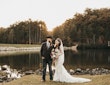 Bride Wearing Lacey Sheath Long Sleeve Wedding Dress Called Francesca By Maggie Sottero Holding Floral Bouquet With Groom Near Water