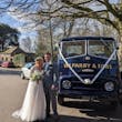 Bride In Long Sleeve Lace Wedding Dress Called Iris By Rebecca Ingram With Groom In Front Of Vintage Car