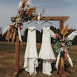 Two Maggie Sottero Wedding Dresses Hanging From A Decorated Post
