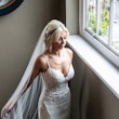 Bride stood by window wearing wedding dress called Juanita.