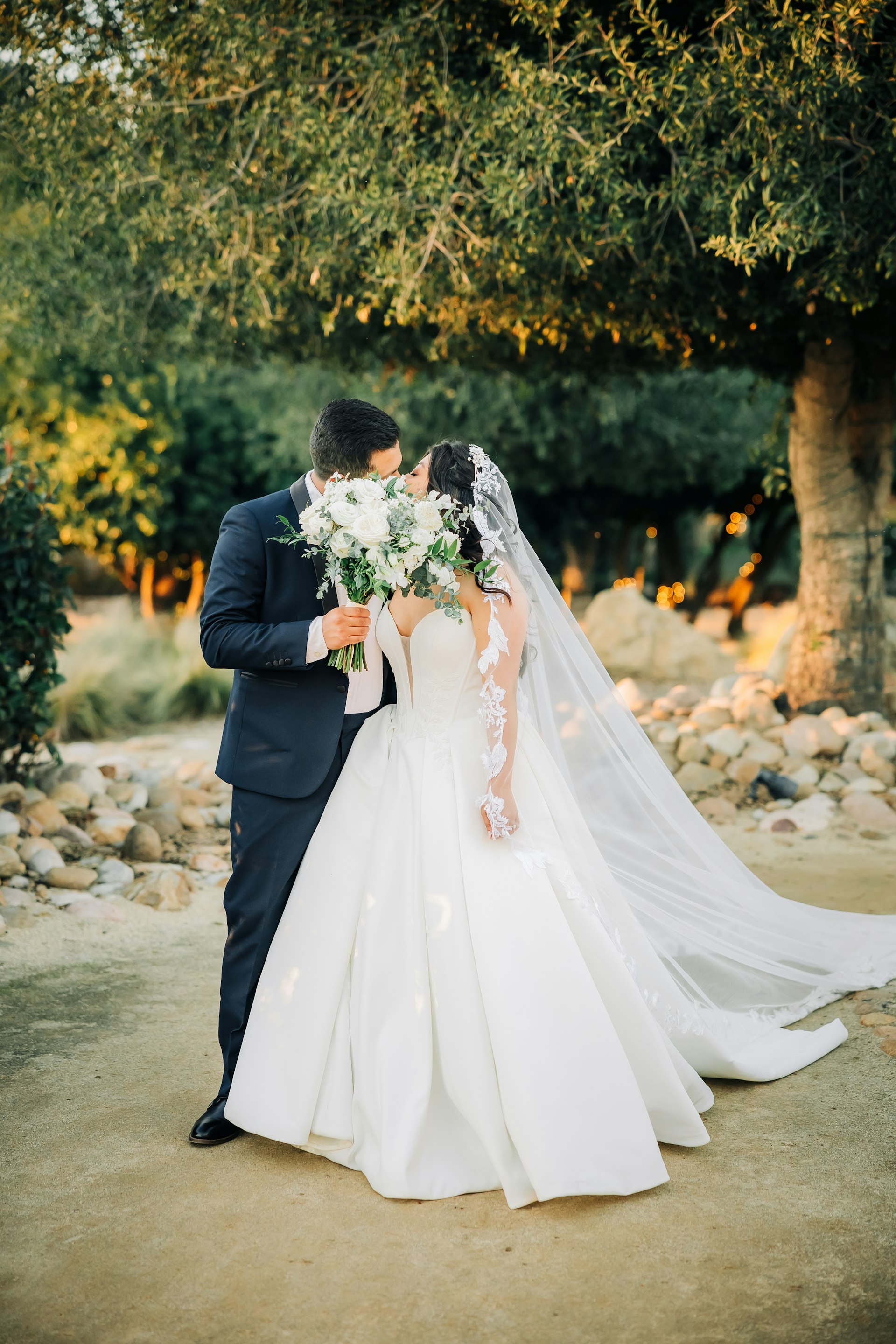 Bride Wearing Sexy Ballgown Wedding Dress Called Derrick By Maggie Sottero Kissing Groom Behind A Bouquet