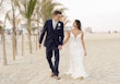 Groom Holding Hands with Bride Walking on Beach Wearing Wedding Dress called Tuscany by Maggie Sottero.