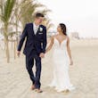 Groom Holding Hands with Bride Walking on Beach Wearing Wedding Dress called Tuscany by Maggie Sottero.
