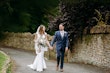 Newlyweds walking on a path looking at each other hand in hand.