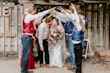 Bride Wearing Simple Fit And Flare Wedding Dress Called Josie By Rebecca Ingram Kissing The Groom Under A Bridal Party Archway