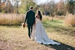 Bride Wearing Floral Ballgown Wedding Dress Called Derrick Marie Holding Hands Walking With Groom In A Field