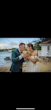 Bride And Groom Sharing A Coconut Drink on The Beach. Bride Wearing Tulle Wedding Dress With 3D Floral Details Called Mirra By Maggie Sottero