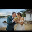 Bride And Groom Sharing A Coconut Drink on The Beach. Bride Wearing Tulle Wedding Dress With 3D Floral Details Called Mirra By Maggie Sottero