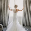 Back view of bride opening curtains wearing wedding dress called Alistaire.