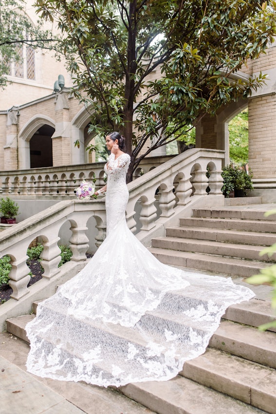 Bride wearing dress called Tuscany Royale standing on steps with train cascading them.