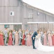 Wedding party in salmon and grey colors cheer as groom kisses his bride.