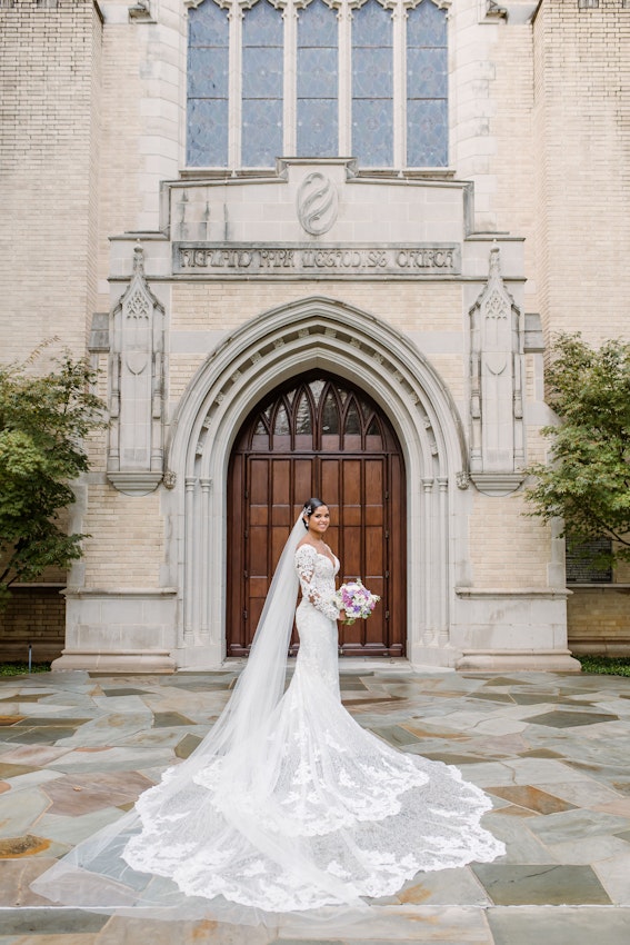 Bride standing outside beautiful old church building wearing dress called Tuscany Royale.