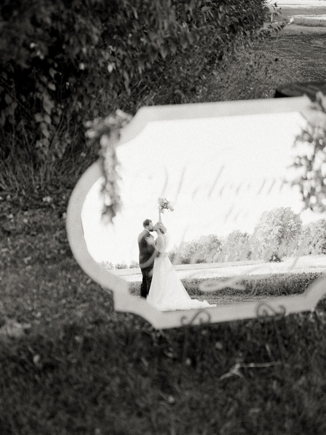 Bride and groom kissing in reflection of wedding sign.