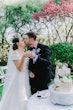 Bride Wearing Off-The-Shoulder A-Line Wedding Dress Called Coral By Rebecca Ingram Cutting The Cake With Groom