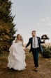 Bride Wearing Square Neck Long Sleeve Floral Wedding Dress Called Sawyer By Sottero And Midgley Walking With Groom Holding Her Bouquet