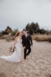 Bride Wearing Beaded Fit-n-flare Wedding Dress Called Jonah Lane By Sottero And Midgley Walking On The Beach Hand In Hand With Groom