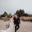 Bride Wearing Beaded Fit-n-flare Wedding Dress Called Jonah Lane By Sottero And Midgley Walking On The Beach Hand In Hand With Groom