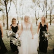 Bride Walking With Bridesmaids Wearing Wedding Gown Called Raelynn by Rebecca Ingram