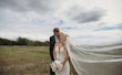 Bride and groom kissing while the veil flows in the wind.