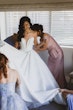 Bride wearing Derrick by Maggie Sottero being zipped up by her bridesmaids