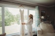 Bride admiring her dress hanging in the window.