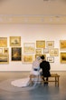 Bride wearing Mitchell Marie Vida by Maggie Sottero sitting with her husband in a museum