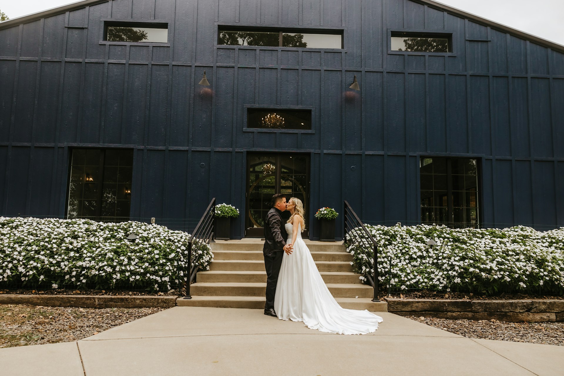 Bride Wearing Aline Satin Wedding Gown Called Scarlet By Maggie Sottero Kissing Groom In Front Of A Black Building