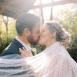 Bride and groom kissing while veil adorned with pearls cascades their shoulders.