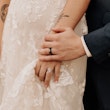 Close up of groom's ring hand on top of the brides.