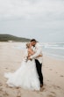 Bride wearing Indiana by Maggie Sottero kissing her husband on the beach