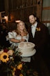 Bride wearing Juniper wedding dress by Sottero and Midgley cutting the cake with her husband