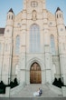 Full view of large church building with newlyweds sat on the steps.