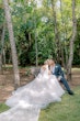 Bride kissing her groom on a bench near the trees.