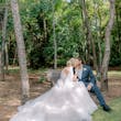 Bride kissing her groom on a bench near the trees.