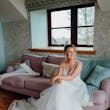 Bride wearing Lettie wedding dress by Rebecca Ingram sitting on a couch