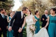 Bride and groom kissing with wedding party surrounding them.