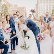 Groom kissing bride as wedding party celebrates with spraying champagne and cheering.