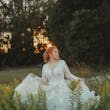 Bride Wearing Lace Long-Sleeve Wedding Gown Called Raphael By Maggie Sottero Walking Through A Field